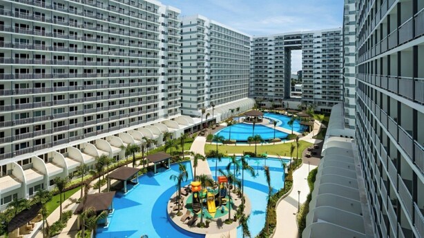 Un hôtel de grande hauteur doté de nombreux balcons, d’une piscine centrale et d’un espace de jeux pour enfants.