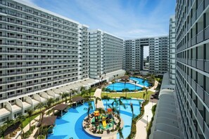 A high-rise hotel with multiple balconies, a central swimming pool, and a children's play area.