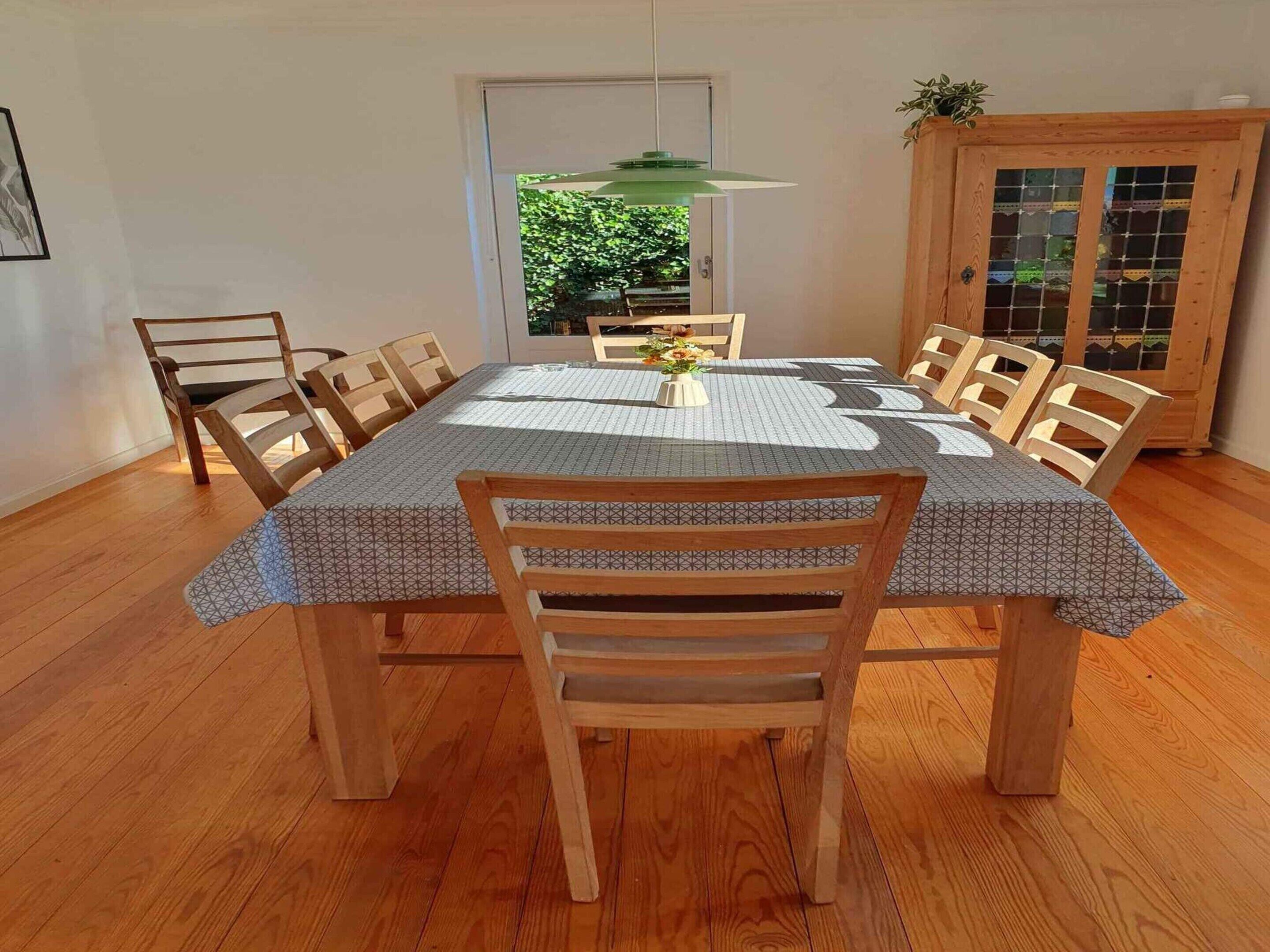 A dining area with a wooden table and chairs, a patterned tablecloth, and a green hanging light fixture.