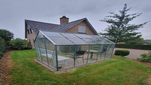 Une serre dotée d’une toiture et de parois en verre, comprenant un banc et une table.
