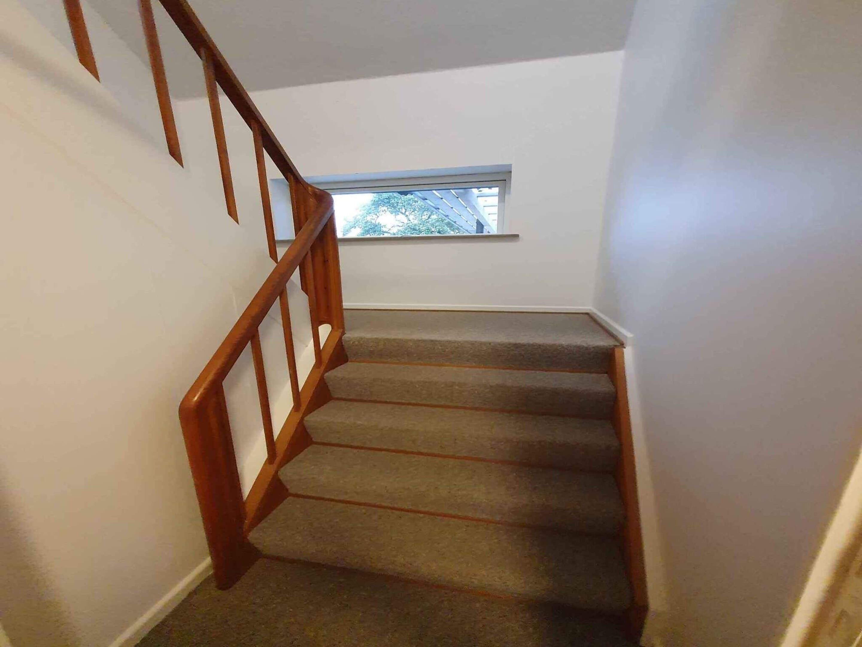 A carpeted staircase with wooden railings leading to a landing with a window.
