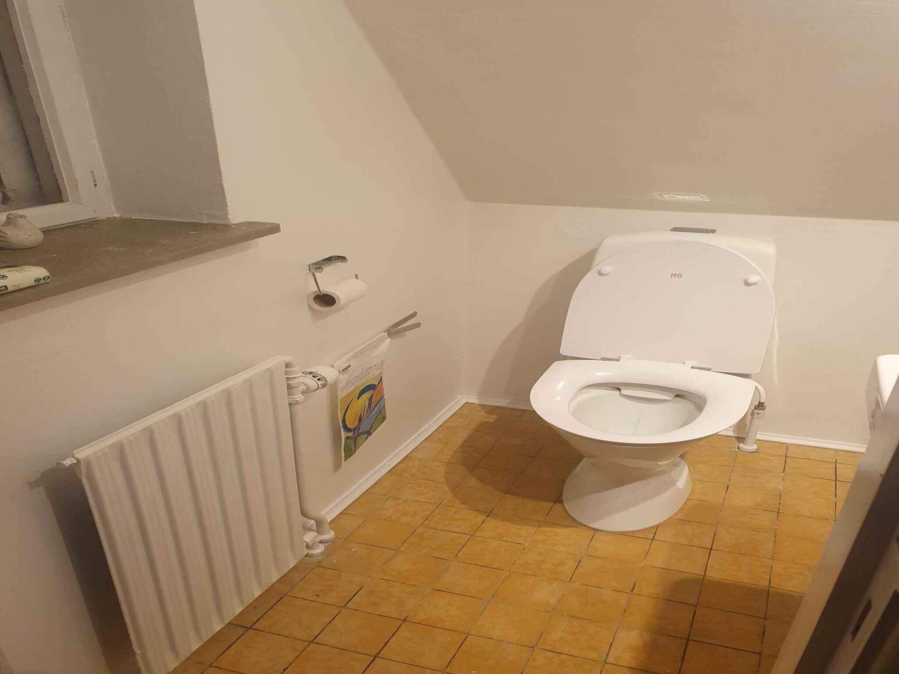 A small bathroom with a toilet, a radiator, and a towel hanging on the wall.