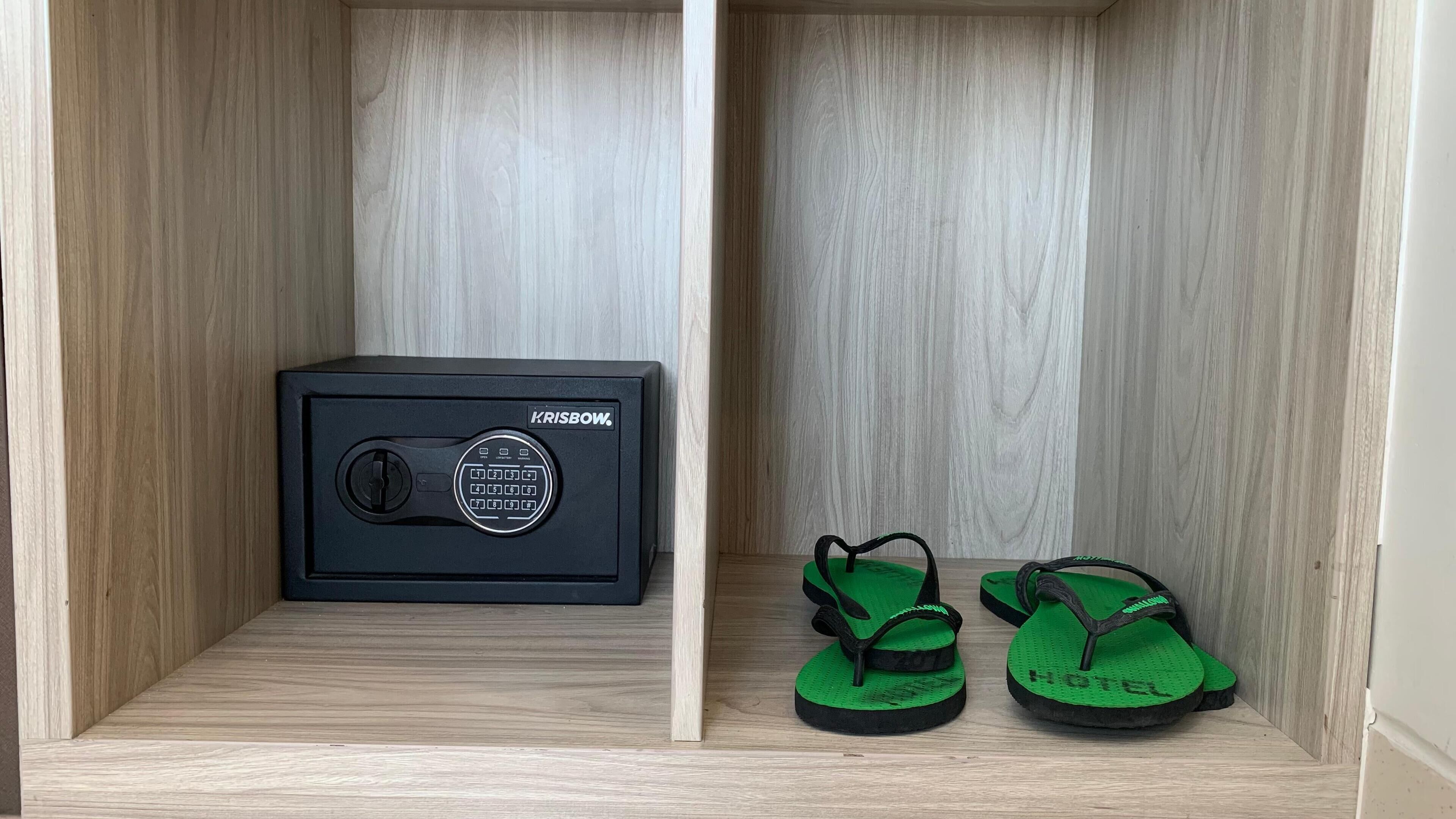 A wooden cabinet with a black safe and green flip-flops inside.