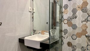 A bathroom with a white sink, a glass shower enclosure, and a wall with hexagonal patterned tiles. - The Baliem Hotel (Jimbaran)