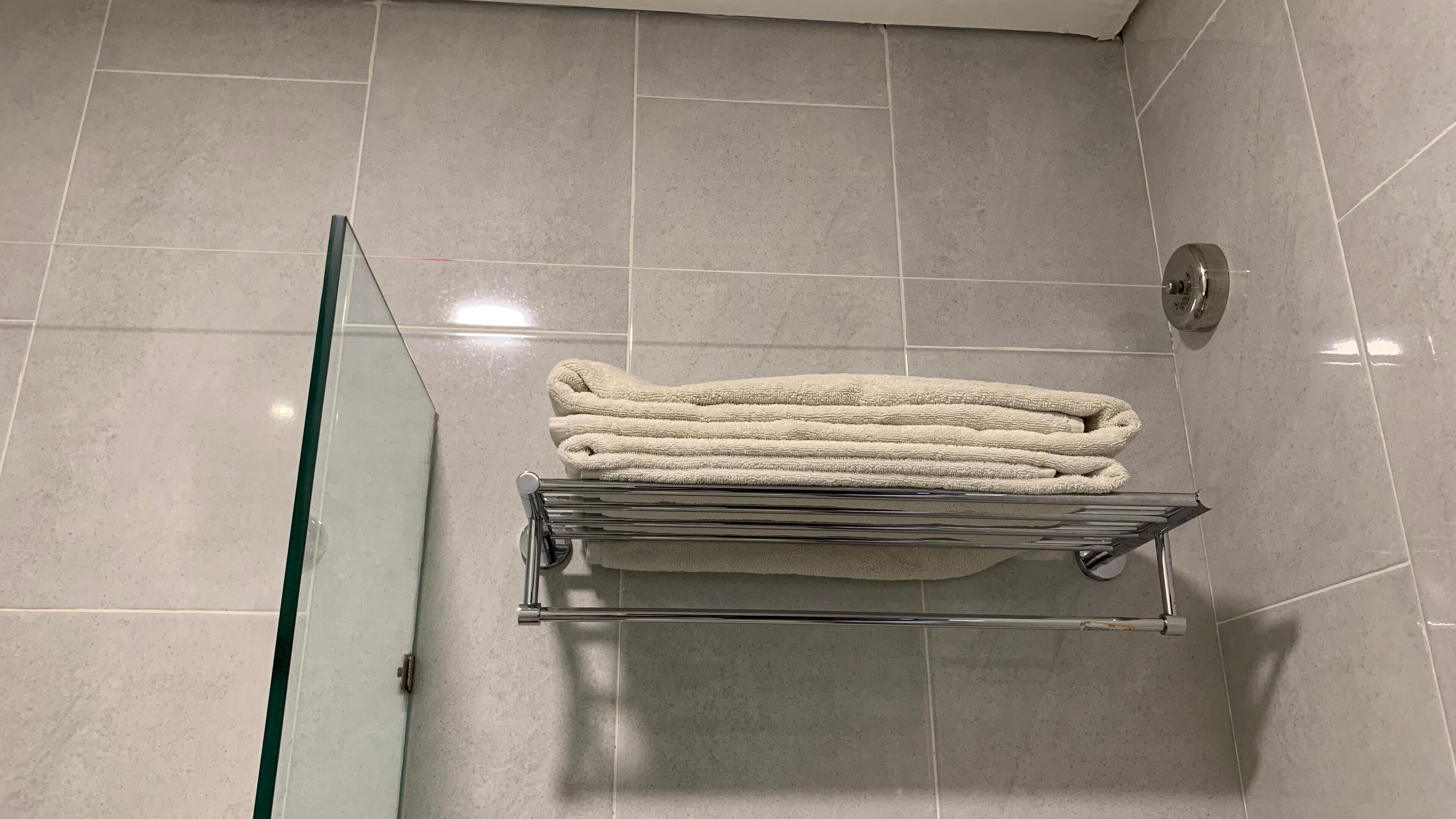 A bathroom with a glass shower door, a towel rack with folded towels, and tiled walls.