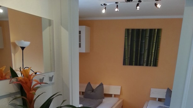 A modern bedroom with two single beds, a large mirror, a potted plant, and a bamboo wall panel. - Vacation apartment on Lake Starnberg In the town center, just a few minutes from the lake (Seeshaupt)