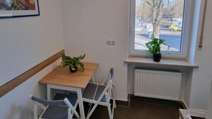 A small, modern room with a wooden table and two white chairs, a potted plant on the windowsill, and a framed abstract painting on the wall. - Vacation apartment on Lake Starnberg In the town center, just a few minutes from the lake (Seeshaupt)