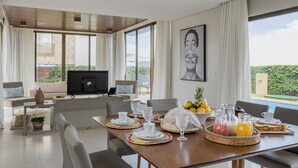 Un salon moderne comprenant un coin repas, un téléviseur à écran plat et une grande fenêtre donnant sur un paysage verdoyant.