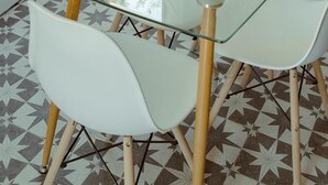 Zona pranzo con tavolo in vetro e sedie bianche, caratterizzata da un pavimento a motivi geometrici e un davanzale in legno.
