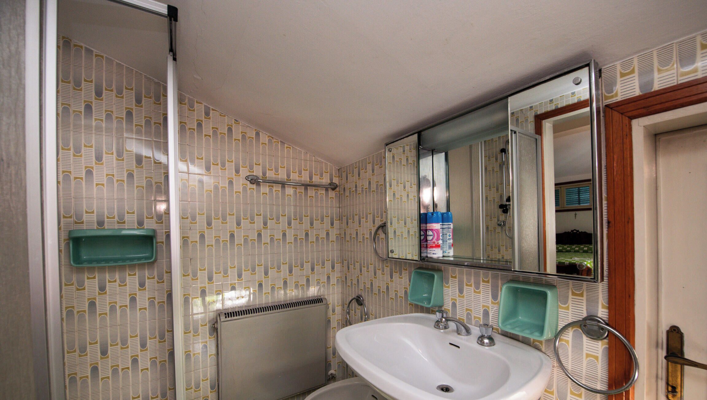 Une salle de bain avec un papier peint à motifs, un lavabo blanc, un bidet et un miroir.