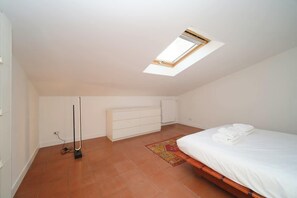 A bedroom with a skylight, a bed, a white dresser, and a radiator.