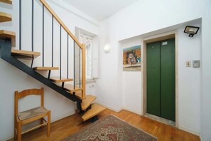 A staircase with wooden steps and black railings, a green door, a chair, and a painting on the wall.
