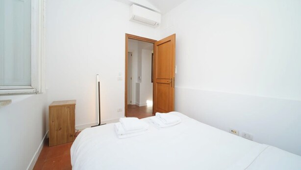 Een slaapkamer met een bed, een houten kast, een staande lamp en een deur naar een andere kamer.