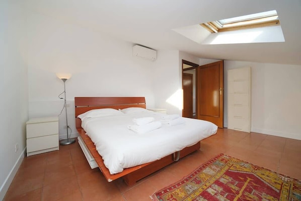 Ein Schlafzimmer mit Bett, Nachttisch, Lampe und einem Oberlicht.