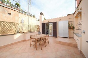Un patio con una mesa y sillas de madera, una puerta corrediza y un armario blanco.