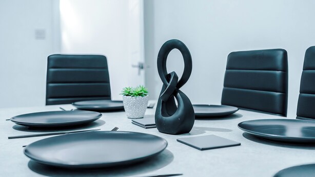 Un salón de conferencias con una mesa moderna dispuesta para una reunión, con sillas negras, una planta en maceta y una escultura negra original.