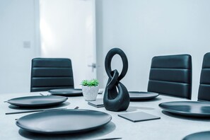 A conference room with a modern table set for a meeting, featuring black chairs, a potted plant, and a unique black sculpture. - Cosy 2 bed house - 15 minutes from City (Manchester)