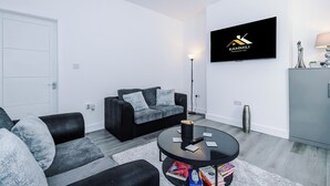 Una sala de estar moderna con un sofá negro, un sofá gris, una mesa de centro redonda y un televisor de pantalla plana montado en la pared.