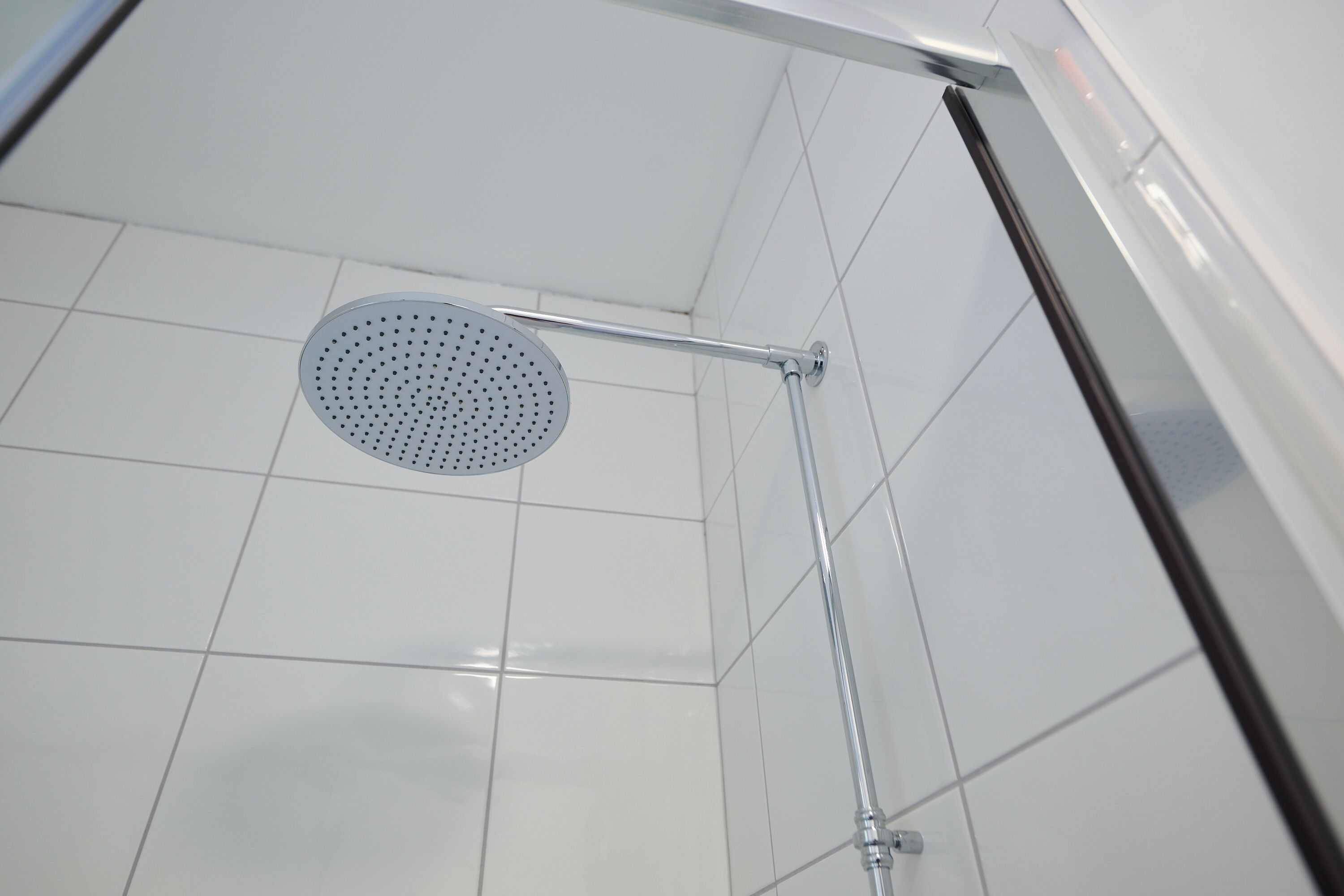 Ducha con desagüe de techo perforado, paredes de azulejos y barra de ducha metálica.