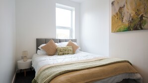 Ein ordentlich eingerichtetes Schlafzimmer mit Bett, Nachttisch, Lampe und Fenster.