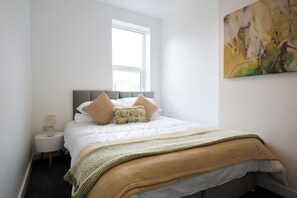 A neatly arranged bedroom with a bed, a bedside table, a lamp, and a window.