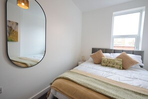 Ein Schlafzimmer mit einem Bett, einem großen Spiegel, einem Fenster und einem Bild an der Wand.