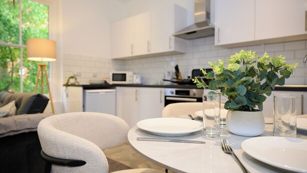 Eine moderne Küche mit weißen Schränken, einem Esstisch komplett mit Geschirr, Gläsern und Besteck, und einem Blumentopf auf dem Tisch.
