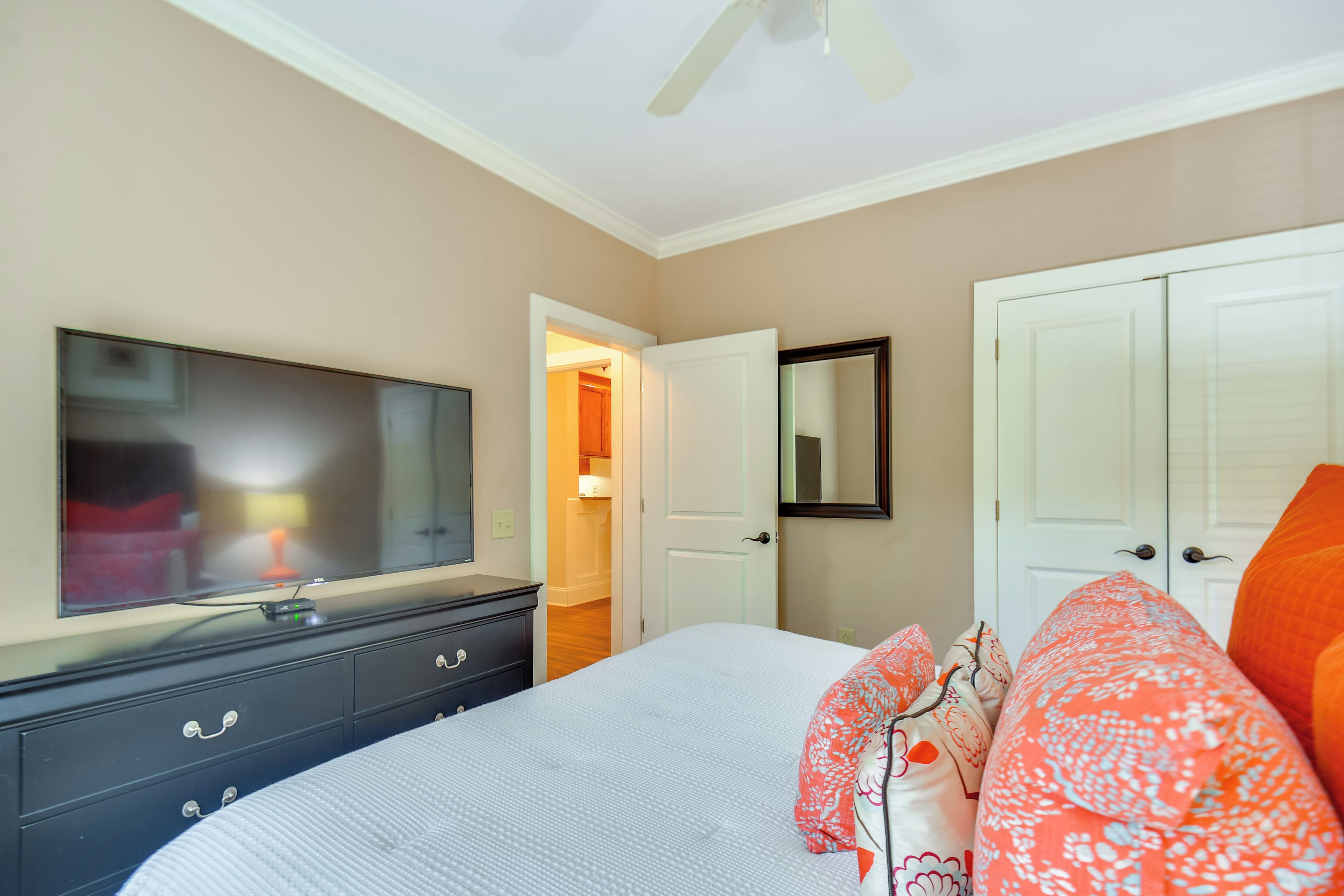 A bedroom with a bed, a TV, a dresser, a closet, and a door leading to another room.