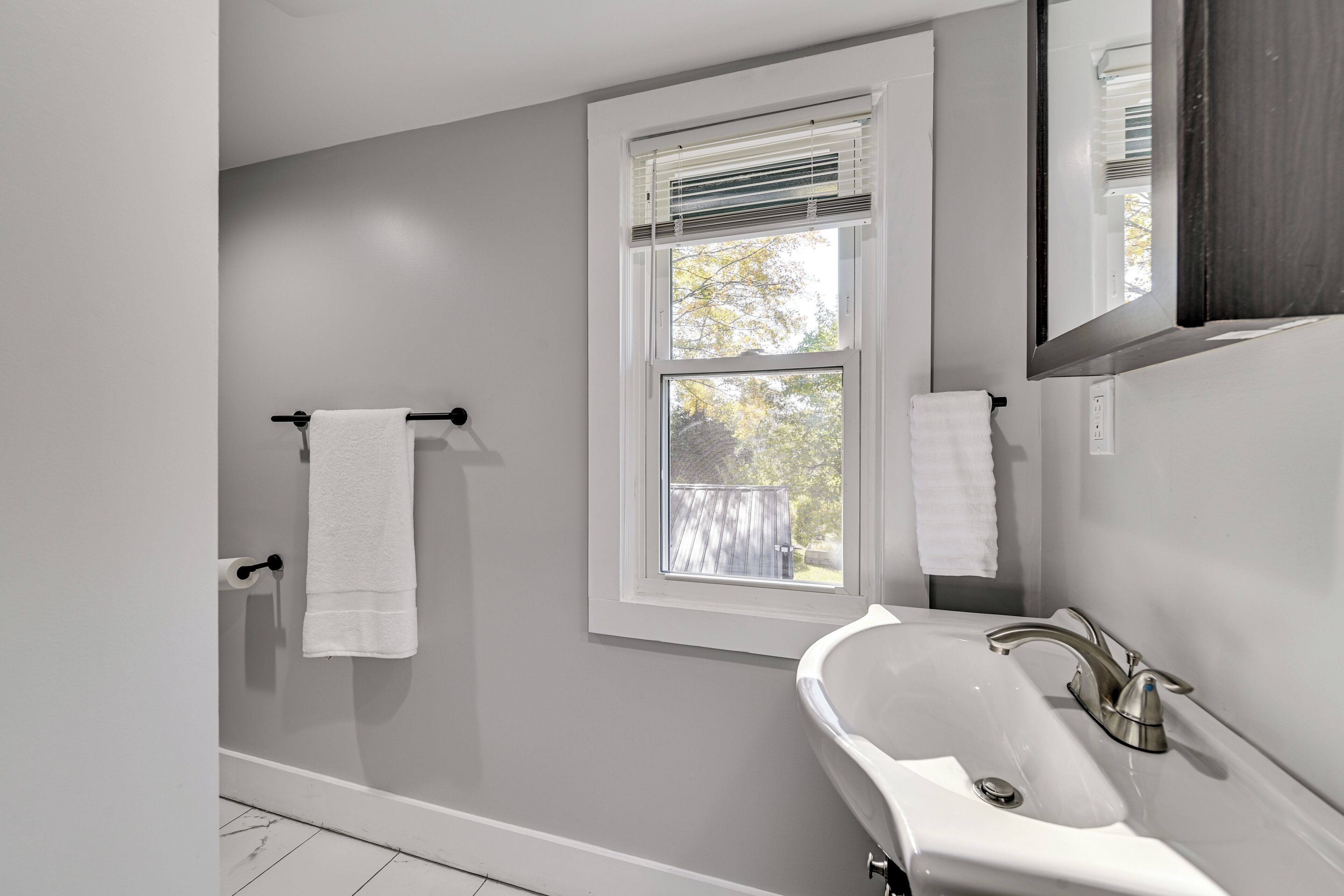 A bathroom with a white sink, a window with blinds, and a towel rack.