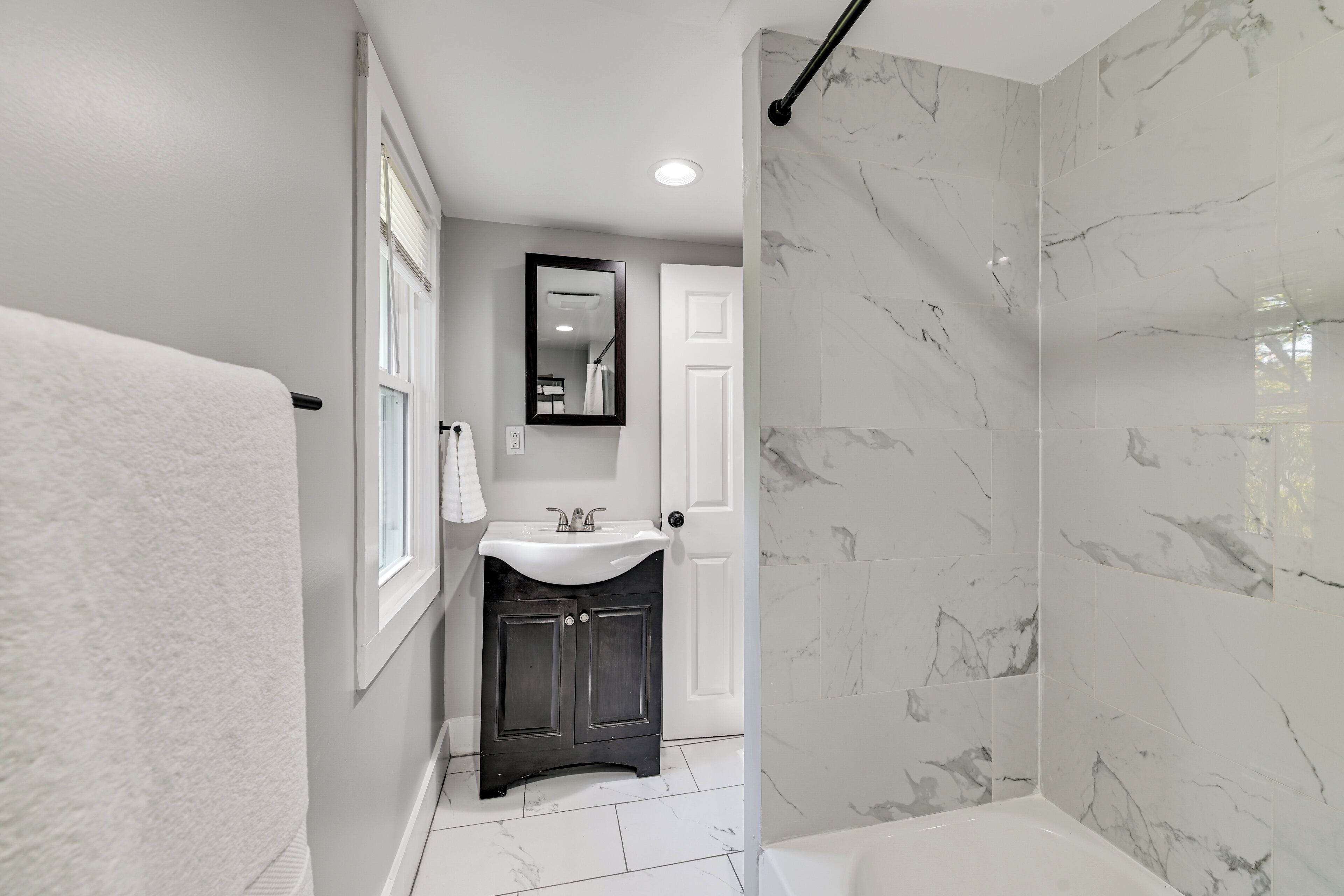 A bathroom with a white bathtub, a dark vanity with a sink, and marble walls.
