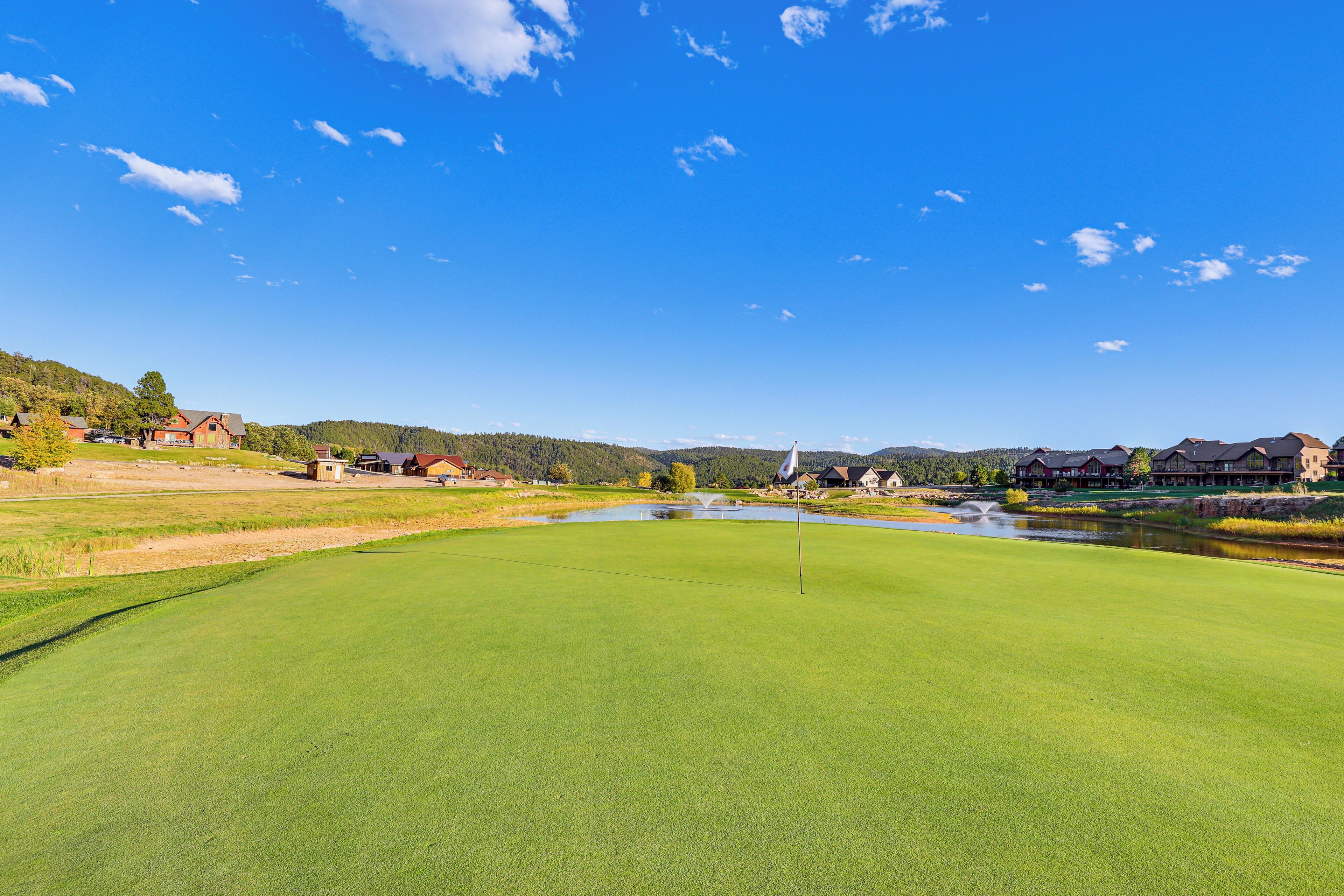 A golf course with a pond, surrounded by houses and hills.