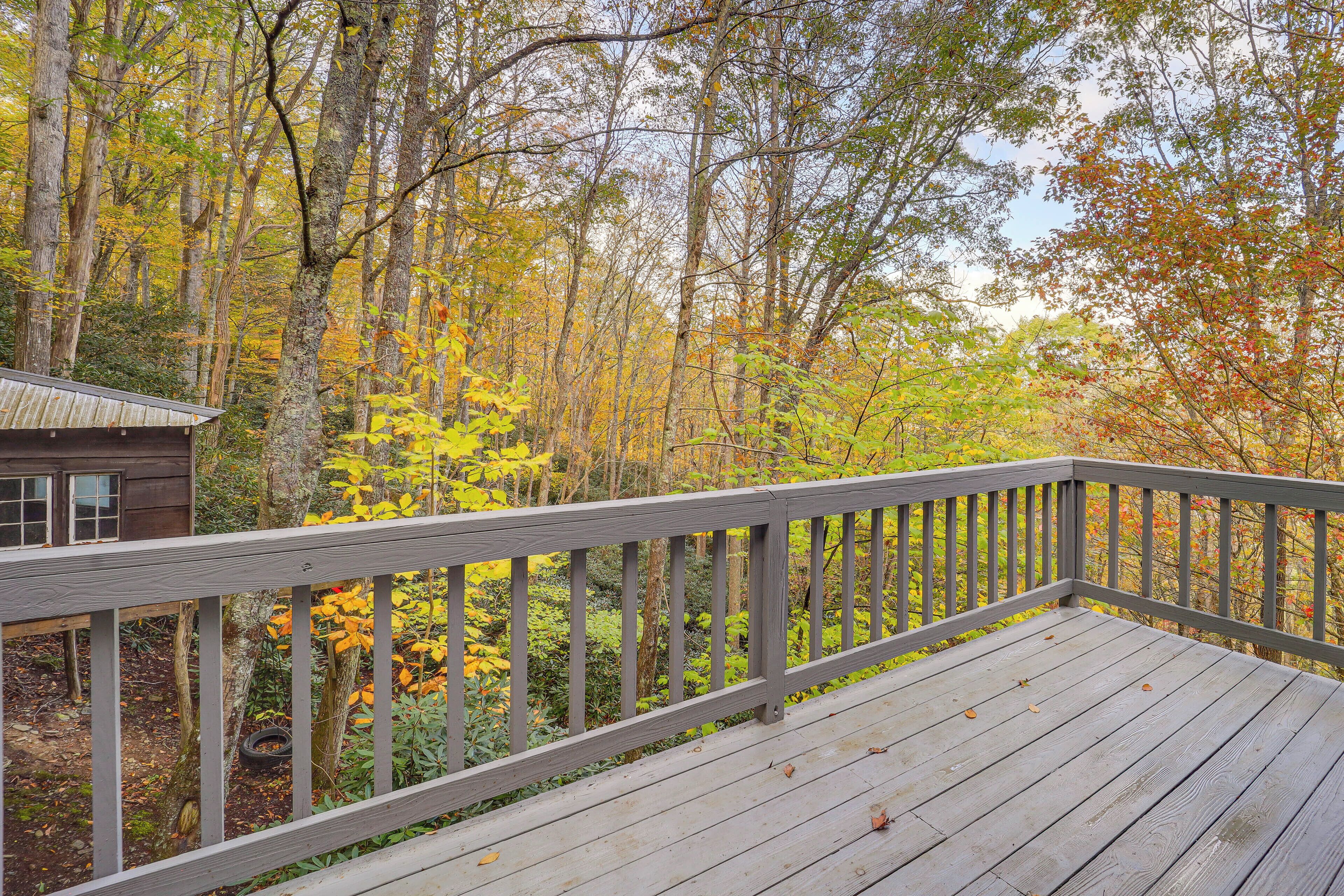 A wooden deck with a railing overlooking a forested area with autumn foliage.