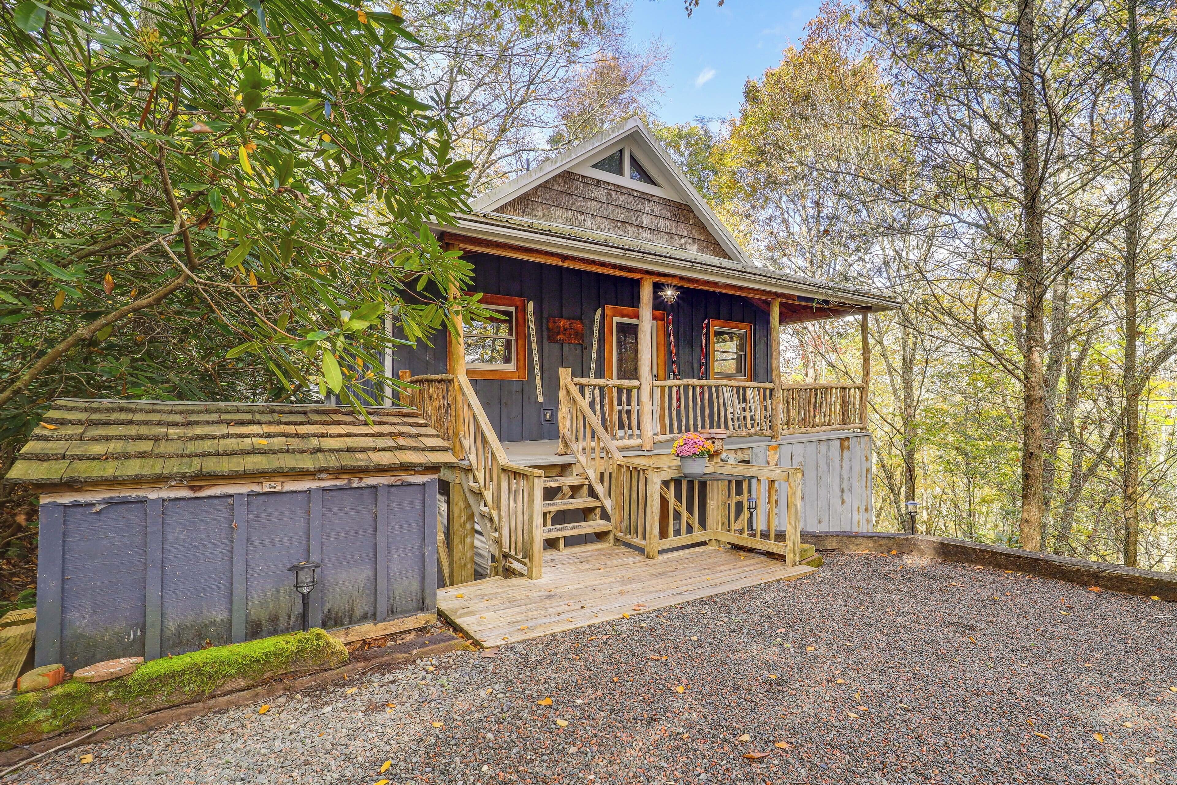 A rustic cabin with a wooden deck, a porch, and a gravel driveway.
