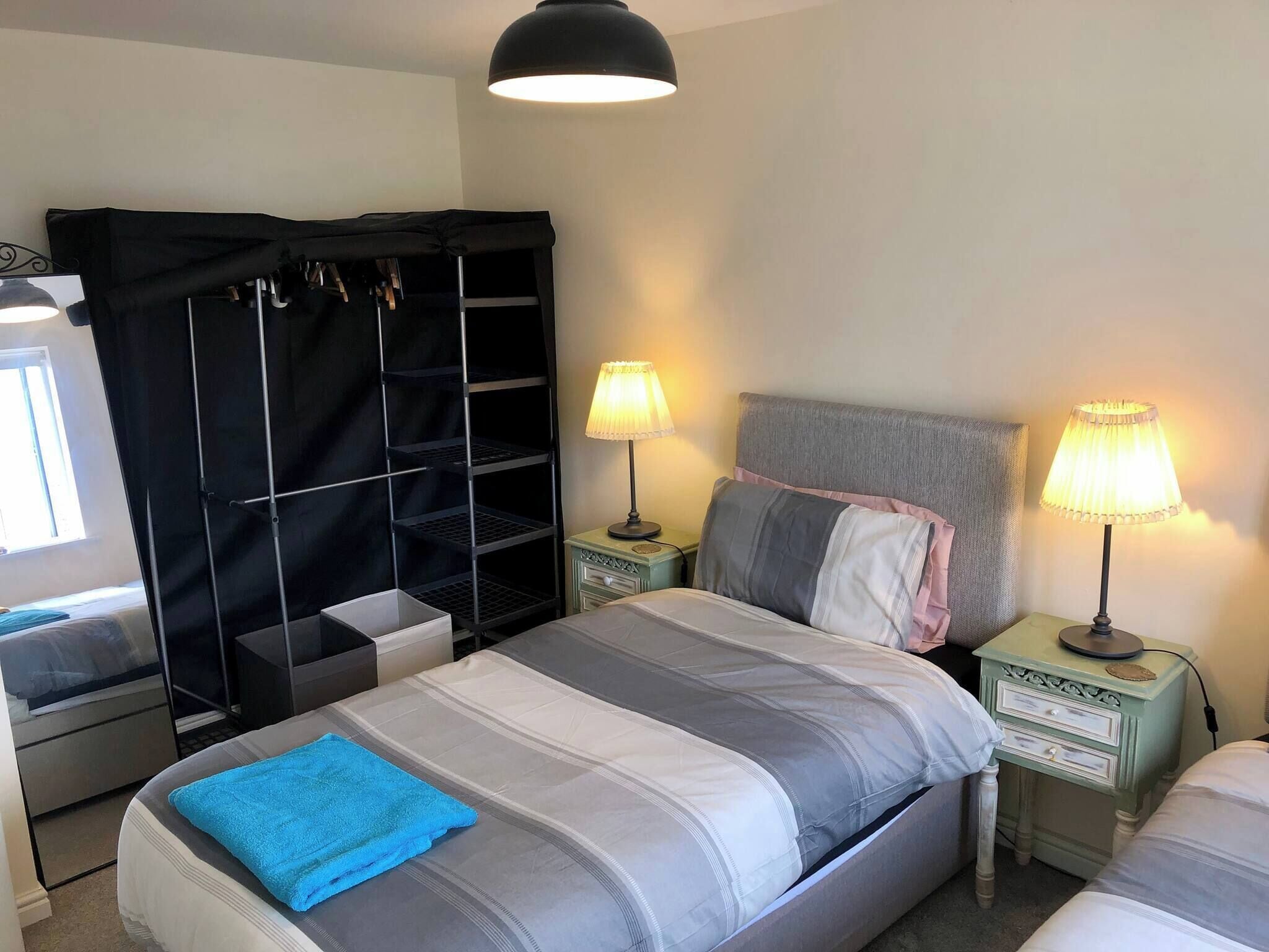 A bedroom with a bed, two bedside tables with lamps, a wardrobe, and a window.