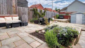 Un jardin avec une terrasse, un espace salon extérieur et un potager.