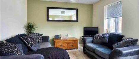 A living room with two sofas, a coffee table, a TV, and a window with blinds.