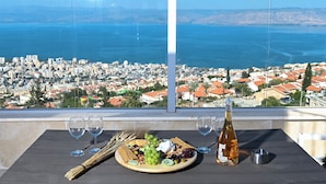 A table with a plate of food, wine glasses, and a bottle of rosé wine, overlooking a city and sea view. - vila Selavi (Tiberias)