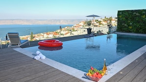 A pool with a view of the sea, a red inflatable ring, a bottle, glasses, and fruit on the edge. - vila Selavi (Tiberias)