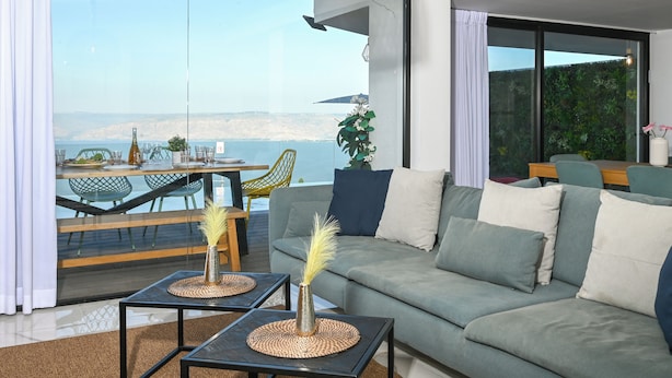 A modern living room with a sofa, a dining table, and chairs. There is a view of the sea and a mountain in the background. - vila Selavi (Tiberias)