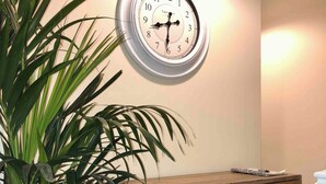 A room with a wooden desk, a potted plant, and a wall-mounted clock. - Entire Two Bedroom Detached Coach House (Exeter)