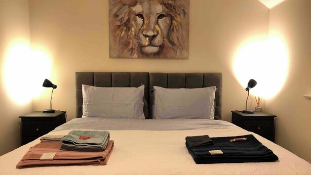 A neatly made bed with a quilted cover, two pillows, and a folded blanket on a nightstand. There is a painting of a lion on the wall above the bed. - Entire Two Bedroom Detached Coach House (Exeter)