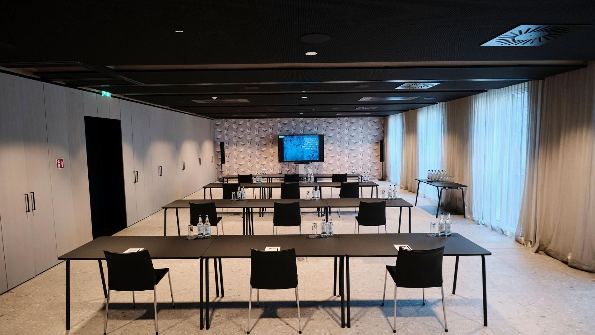 Una sala de conferències amb una taula llarga, cadires, un televisió de pantalla plana i un altaveu.