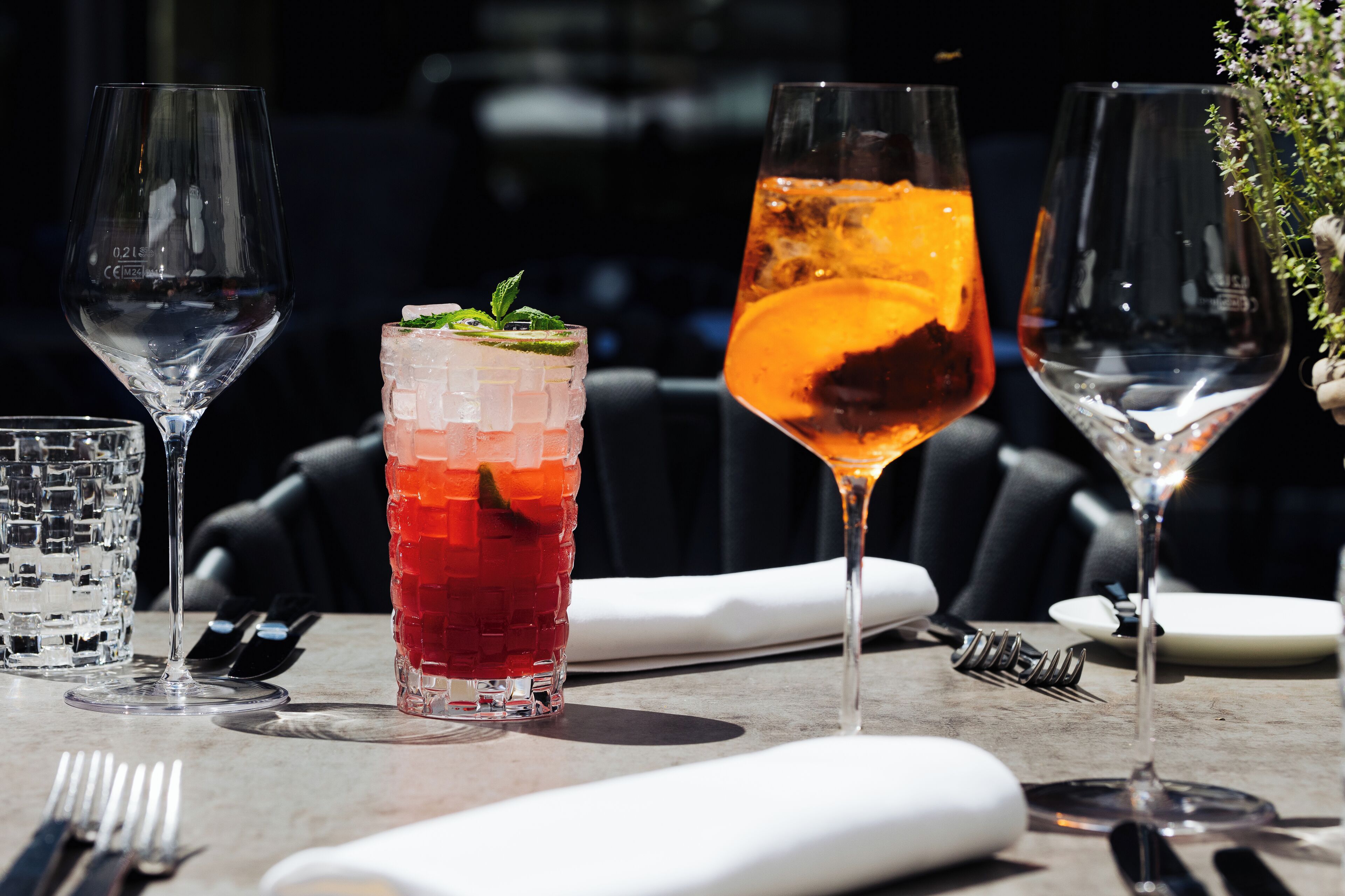 A table with various glasses of beverages, including a tall glass with a red drink and a shorter glass with a layered drink.