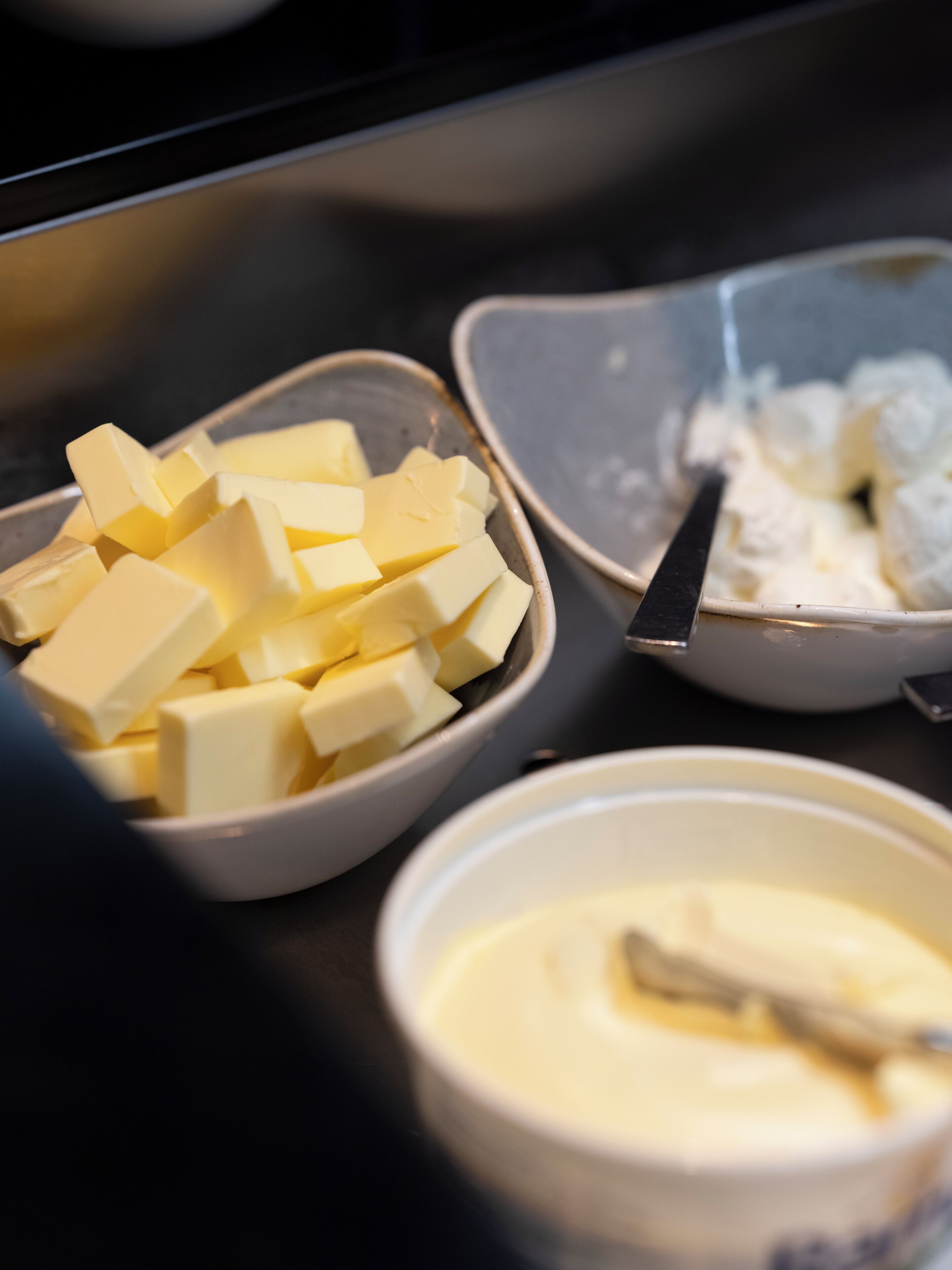 Una mesa de buffet con tres recipientes que contienen cubos de mantequilla, crema batida y una salsa cremosa.