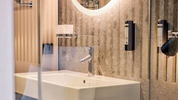 A modern bathroom with a large rectangular sink, a round mirror with a light, and a glass shower enclosure.