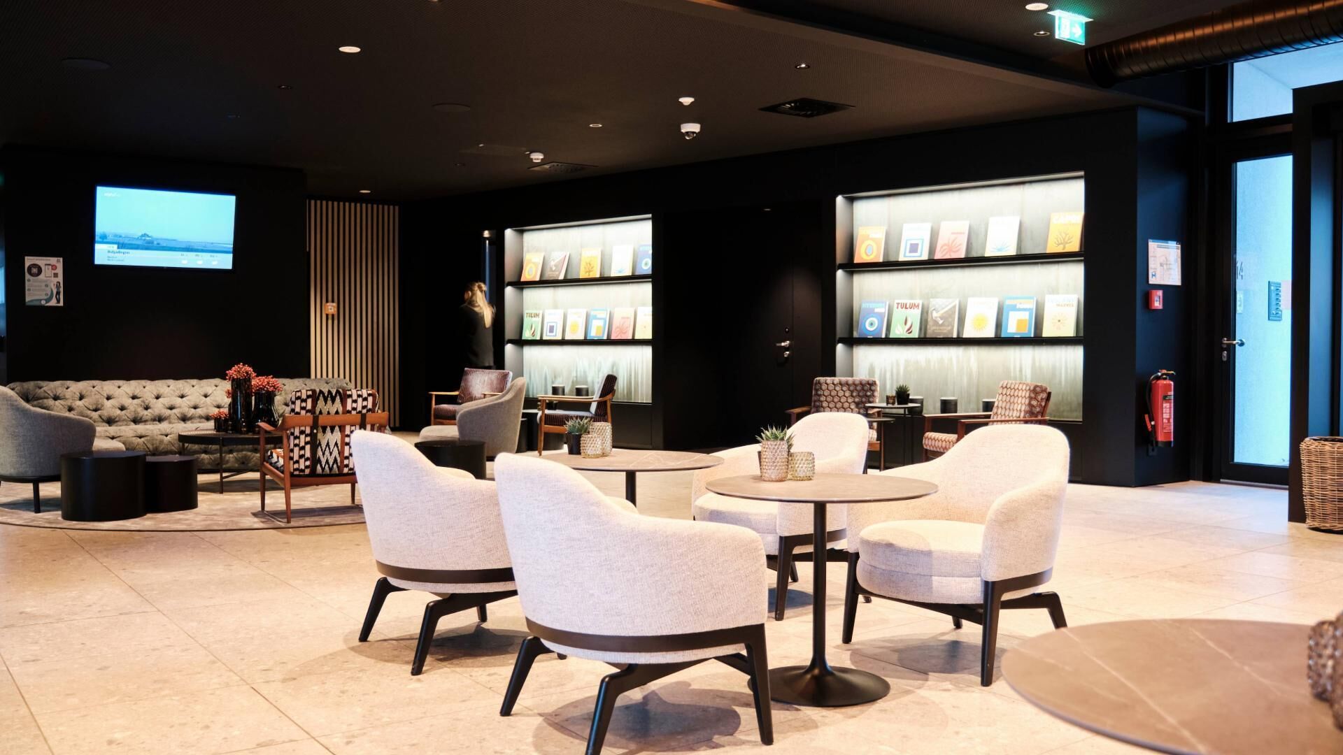 A modern lounge area with sofas, armchairs, and a coffee table, featuring a fireplace and a wall with framed pictures.