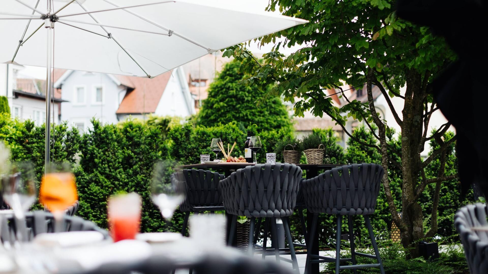 Un espacio de comedor al aire libre con una mesa dispuesta para dos personas, rodeado de vegetación y una sombrilla blanca.