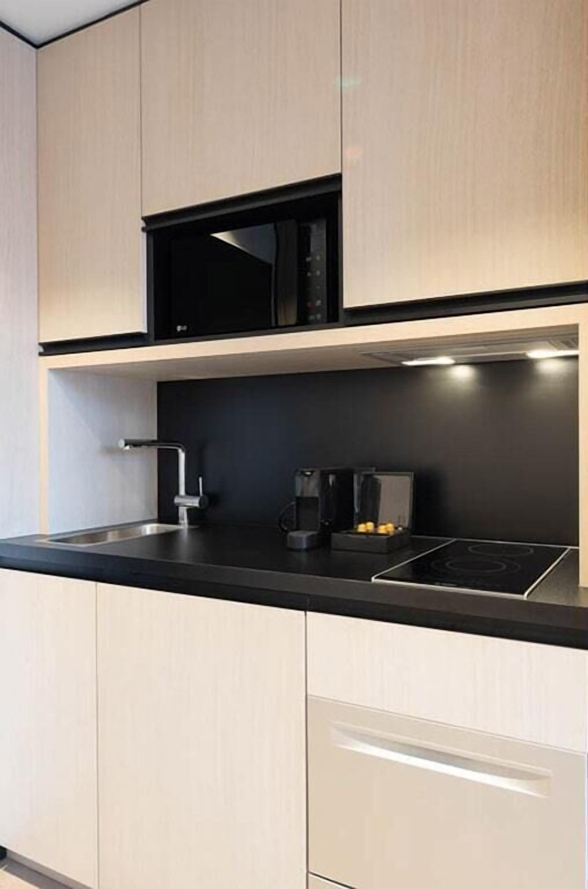A modern kitchen with light wood cabinets, a black countertop, a built-in microwave, a coffee maker, and a stainless steel sink.