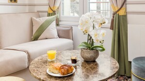 Une table ronde en marbre, sur laquelle sont disposés des aliments pour le petit-déjeuner, un canapé et une orchidée en pot.