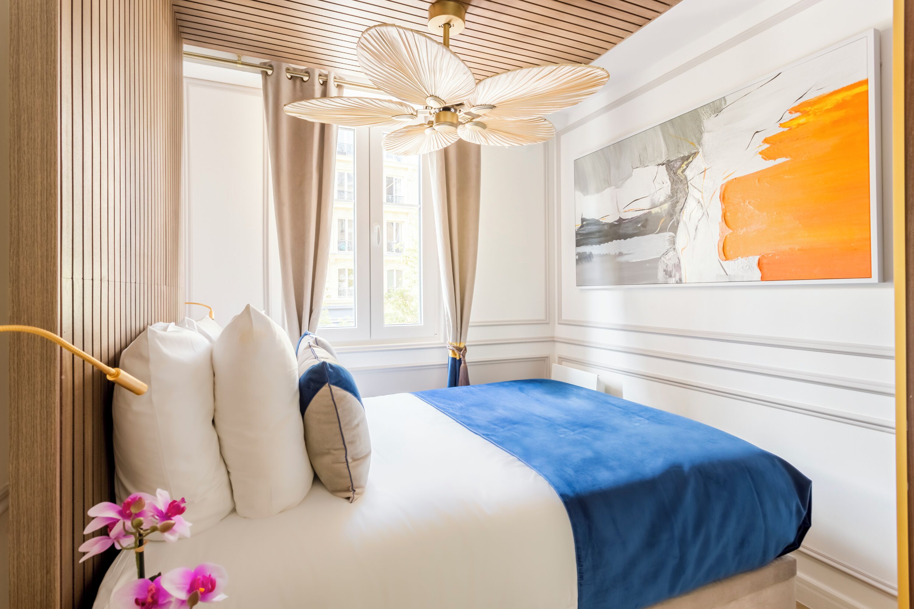 A bedroom with a bed, a ceiling fan, a window with curtains, and a painting on the wall.